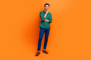 Full body cadre of young boss expert businessman touch chin wear green shirt blue pants classic shoes isolated on orange color background
