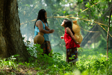 Two girls Asian women with traditional clothing stand in the rainforest. They had fun playing together before assisting Grandpa in catching fish in a nearby lake.
