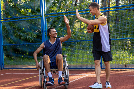Unidentified man in wheelchair after playing basketball game giving high five to his friend.