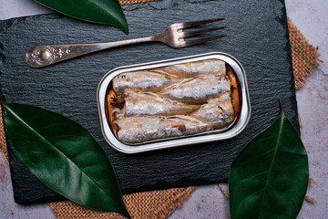 Closeup of can of sardines in olive oil on a black slate stone,view from above.