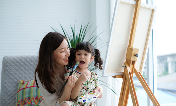 Cute little girl has fun mixing and painting with her young asian mother teaching beside her. - Powered by Adobe