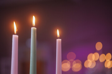 Three white candles with a purple background and orange lights. Concept of creating a cozy and...