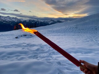 Hand holding torch, winter landscape at twilight in the background.