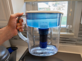 hand holds a water filter pitcher with new cartridge installed that is ready to filter lead and other wastes from drinking water