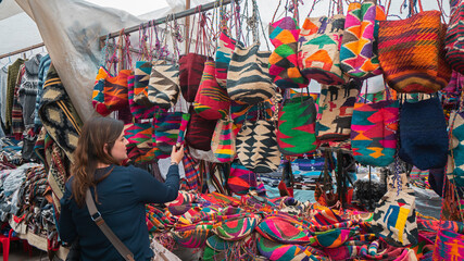 Young Latin American woman comparing Shigras that hang for sale in the Plaza de los Ponchos in the...