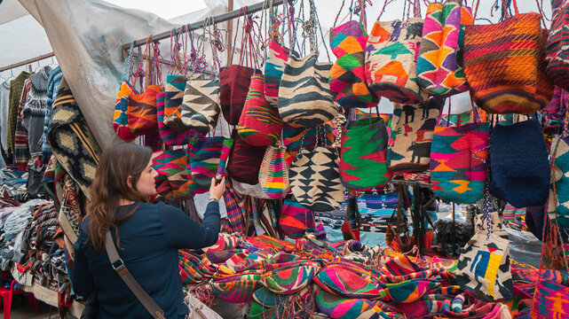 Young Latin American woman comparing Shigras that hang for sale in the Plaza de los Ponchos in the city of Otavalo