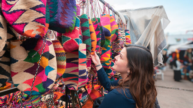 Beautiful young Latin American woman comparing Shigras that hang for sale in the Plaza de los Ponchos in the city of Otavalo