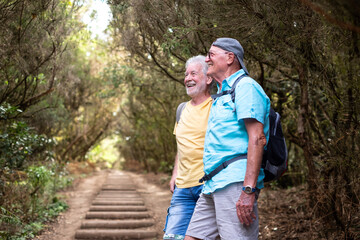 Happy couple of Caucasian senior male friends enjoying trekking day in forest watching nature, relaxed and healthy retirement lifestyle