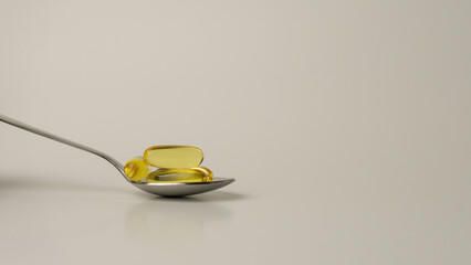A spoon full of Omega-3-rich wild salmon and fish oil capsules presented on a soft off-white background.