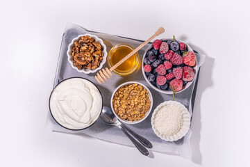 Cooking making Frozen Yogurt Bark background with greek yogurt, fresh berry, granola, honey, chocolate sauce, with baking tray deco. Top view of woman hands cook frozen yoghurt bars