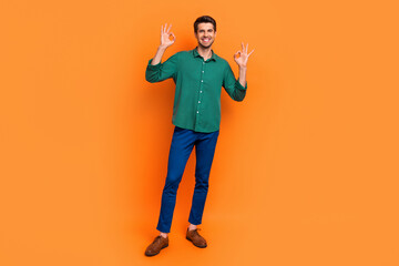 Full length photo of positive confident guy wear green shirt showing two okey gesture isolated orange color background