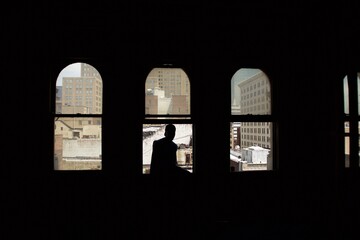 Silhouette of man sitting in the window of an empty apartment building looking out at the skyline in Newark, New Jersey
