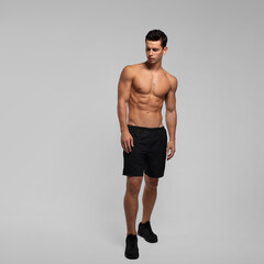 Full length image of a man with an athletic and fit body, with a bare torso, isolated on the grey background.