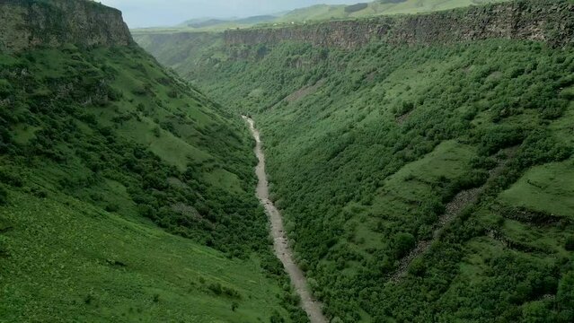 Drone video. Camera flies up from a deep rocky canyon with steep walls. At the bottom of the Dzoraget River near Gnevank Monastery in Armenia. Above is the village of Kurtan.