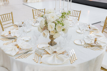 Round table at wedding event for six people with classic dishes, silverware,white table textiles. 