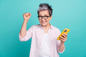 Photo of crazy lady white dyed hair pensioner fist hooray remote work day schedule done with smartphone isolated on cyan color background