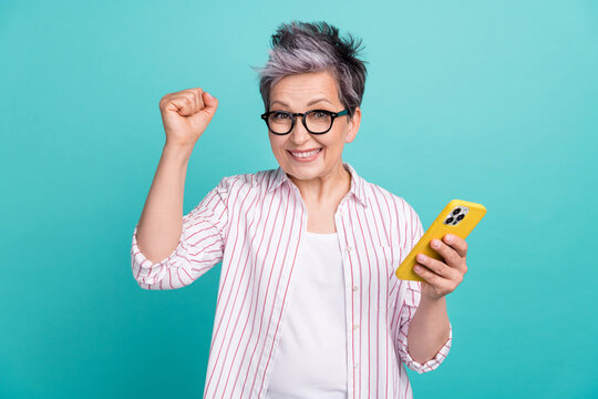 Photo of crazy lady white dyed hair pensioner fist hooray remote work day schedule done with smartphone isolated on cyan color background