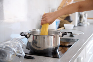 Close-up housewife's hand taking off spaghetti from a container while cooking dinner in the home kitchen