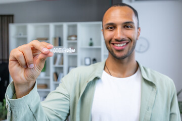 Young handsome man holding aligner standing with a happy face and smiling showing teeth