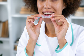 Young woman wearing dentist uniform holding brackets and invisible aligner at clinic