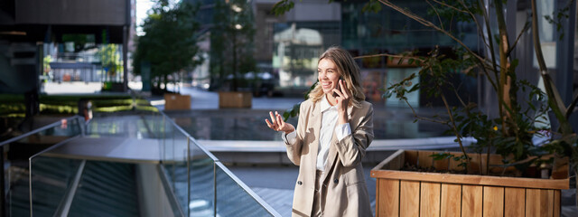 Woman laughs during phone call. Businesswoman talking on her telephone, standing in beige suit...