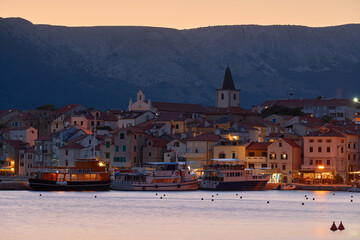 Evening cityscape of the town of Baska on the island of Krk in Croatia. The old town with a promenade by the port. A tourist resort located on the Adriatic Sea with mountains in the background