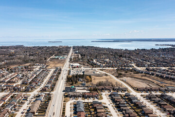 Aerial view of Barrie, Ontario, highlighting dense residential areas adjacent to the expansive, icy expanse of Lake Simcoe. The urban landscape showcases modern homes and infrastructure against a sere