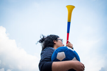 Woman holding blue soccer ball and using vuvuzela to support team in cloudy day 