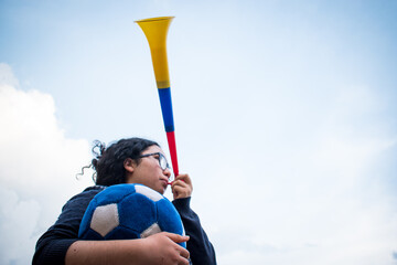Woman holding blue soccer ball and using vuvuzela to support team in cloudy day