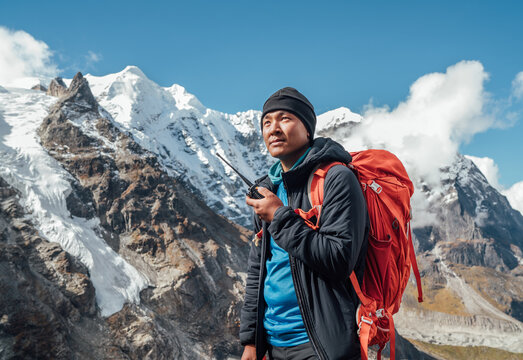 Portrait of Sherpa man with backpack using walkie-talkie for calling rescue helicopter with Mera peak 6476m background.High Himalayas expedition during mount climbing. Traveling, active people concept