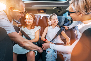 Inside car photo of mother and father fastening with safety auto belts their little daughters girl...