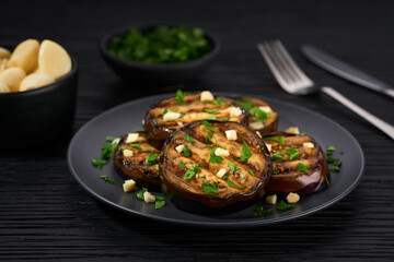 Homemade grilled eggplant with parsley and garlic  on a black table.