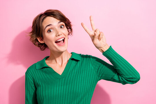 Portrait of satisfied optimistic girlish woman with short hair wear stylish shirt showing v-sign symbol isolated on pink color background