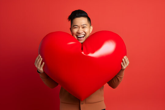 smiling Asian man holding big red heart on red background. Not based on any actual person or scene