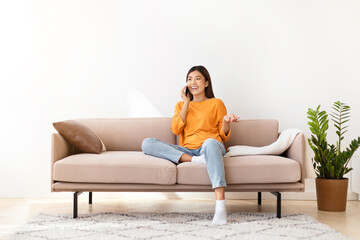 Obraz premium Smiling pretty young asian woman talking on phone at home