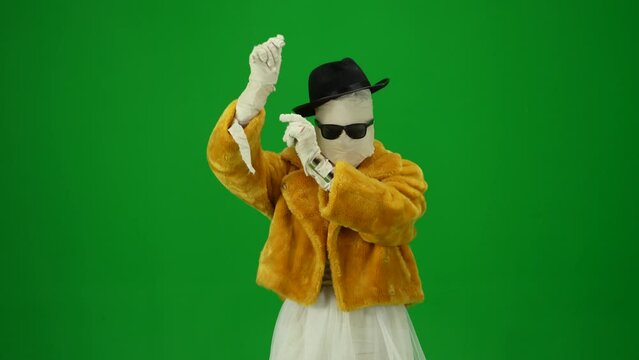 Green screen isolated chroma key video capturing a glamorous mummy dancing in an orange fur coat, hat and sunglasses. Mock up, workspace for your promotion clip or advertisement. Medium size.