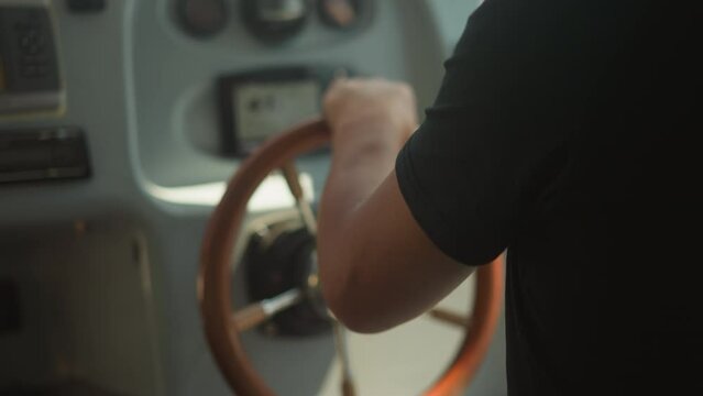 Skilled skipper controls modern yacht with helm in cockpit closeup. Man in black t-shirt sails motor boat on sunny day. Capitain on shift at dashboard