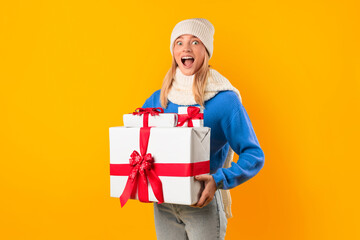 Joyful woman holding Christmas boxes in a yellow studio, exuding excitement and festive spirit