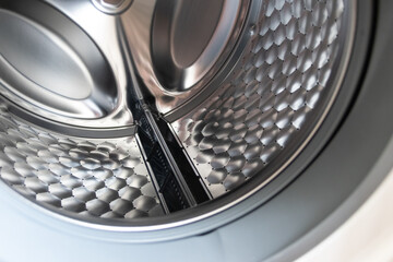 View into washing machine drum inside with stainless steel drum interior shows household equipment for cleaning clothes with dry cleaner and front loader for easy housework laundromat machine empty