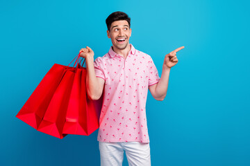 Portrait of astonished guy hold store shop bags look indicate finger empty space ad isolated on...