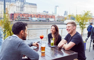 Tuinposter group of friends sitting having a drink talking having a good time outdoors with a view of the city streets © oscargutzo