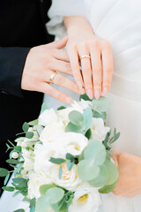 Hands of bride and groom with wedding rings on beautiful bouquet of roses.
