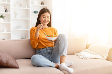 Slim cheerful young asian woman eating healthy salad at home - obrazy, fototapety, plakaty