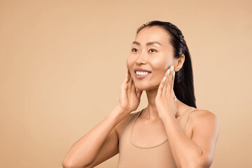 Joyful Asian woman touching face, showcasing clear skin, beige background, free space