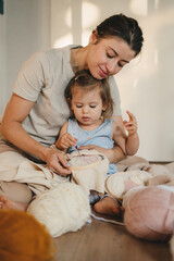 Young mother with her baby girl sitting on the floor at home, embroidering handkerchief. Happy mindfulness concept