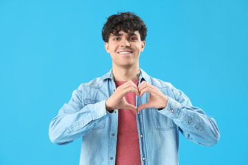 Handsome young man making heart with his hands on light blue background