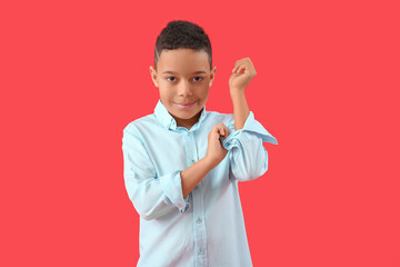Little African-American boy rolling up his sleeve on red background