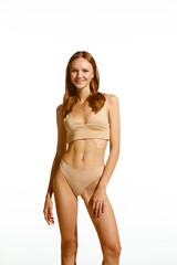 Portrait of pretty young girl with fit, slim, muscular body posing in beige underwear against white studio background. Concept of natural beauty, body and skin care, health, sport, wellness.