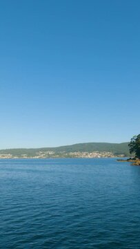 Tranquil waters, azure skies, and the picturesque Ria de Pontevedra unveil in slow motion from a moving boat. A serene summer morning with distant views of Combarro.