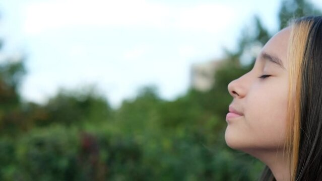 Portrait of a young beautiful preschool girl enjoying a warm summer day outdoors. Cute girl relaxing outdoors on the street, breathing fresh air. Profile of a child's face against the backdrop of a